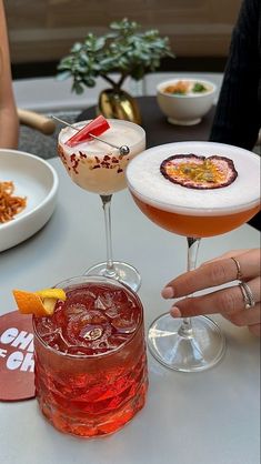 three cocktails sitting on top of a white table next to plates and utensils