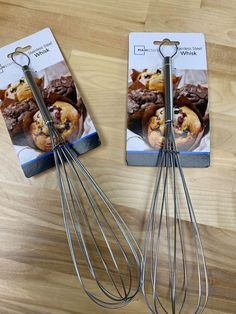 two metal whisks sitting on top of a wooden table next to each other