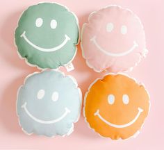 three pillows with smiley faces on them sitting next to each other in front of a pink background