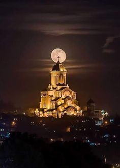 the full moon is setting over a building with lights on it's roof and steeple