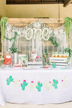 a table topped with cakes and desserts next to a cactus wall hanging from the ceiling