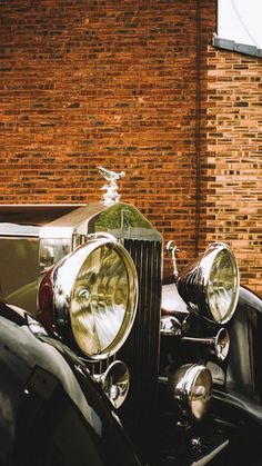 an old car is parked in front of a brick building with its hood ornament