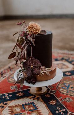 a black and brown wedding cake with flowers on top is sitting on a colorful rug