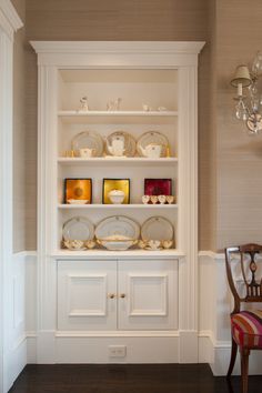 a white china cabinet with plates and cups on it's shelves in a dining room