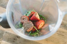 strawberries and spinach in a blender sitting on a wooden table, viewed from above