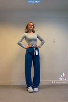 a woman standing in front of a wall with her hands on her hips and wearing blue pants