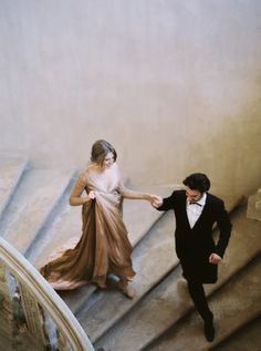 two people in formal wear walking down the stairs together, one holding the hand of the other's hand