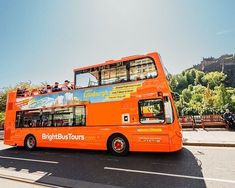 an orange double decker bus driving down the street with people sitting on top of it