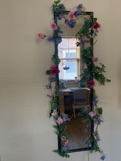 a mirror that has flowers on it in front of a table with a chair and window