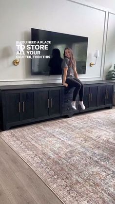 a woman sitting on top of a black entertainment center in front of a flat screen tv