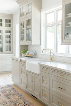 a large kitchen with white cabinets and gold hardware on the doors, windows, and sink