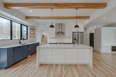 a large kitchen with white cabinets and wood flooring in the middle of an open concept home