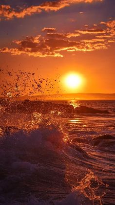 the sun is setting over the ocean with waves crashing in front of an orange and blue sky