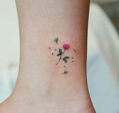 a small flower tattoo on the side of a woman's ankle, with pink flowers and green leaves