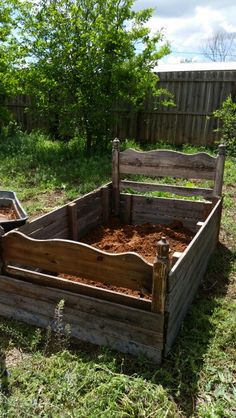 an old wooden bed in the middle of some grass and dirt with trees in the background