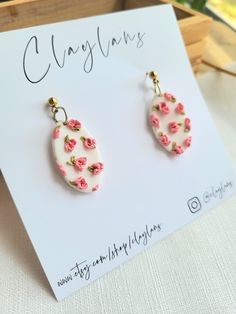 pink and white earrings with flowers on them sitting on top of a card next to a box