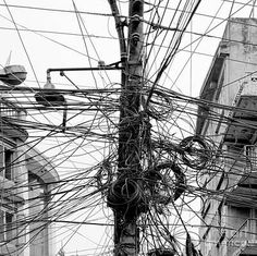 black and white photograph of power lines in an urban area with two people walking on the sidewalk