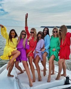 six women in colorful dresses posing on a boat with their arms up and legs spread out