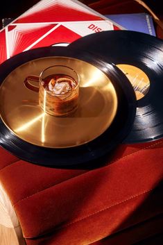 an old record with a drink in it sitting on a red velvet cushion next to other records