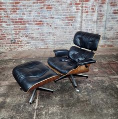 an eames chair and ottoman in front of a brick wall