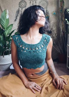 a woman sitting on the floor with her eyes closed wearing a green crochet top