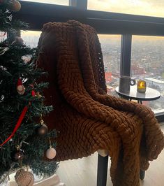 a blanket draped over the back of a chair next to a christmas tree in front of a window