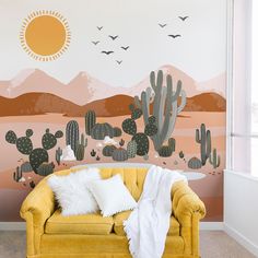 a yellow couch sitting in front of a wall mural with cactus and birds on it