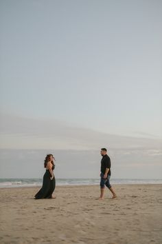 a man and woman standing on top of a sandy beach