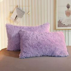 two purple pillows sitting on top of a bed next to a framed photo and wall