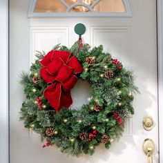 a christmas wreath hanging on the front door with lights and pineconis around it