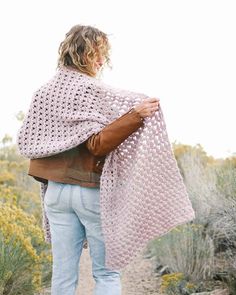 a woman is walking in the desert wearing a pink crocheted shawl