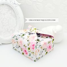 a white box with pink roses on it next to a wallpapered background and an ornate frame