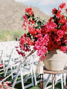 a vase filled with red flowers sitting on top of a wooden table next to white chairs