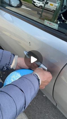 a person is opening the door of a car with a blue object in their hand