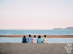 four people sitting on the beach looking out at the ocean