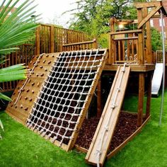 a wooden play set in the grass with a slide and climbing frame attached to it