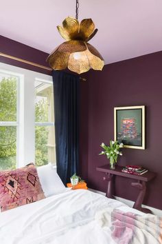 a bedroom with purple walls, white bedding and a hanging lamp above the bed