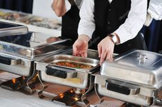 two men in suits are serving food to each other at a buffet table with silver trays