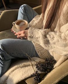 a woman sitting on a chair holding a cup of coffee and berries in her hand