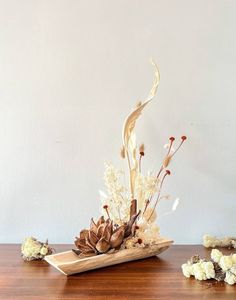 a wooden table topped with a vase filled with white flowers and dried plants on top of it