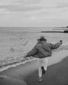 black and white photograph of woman running on beach with seagulls in the background