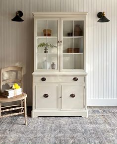 a white china cabinet sitting next to a chair