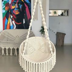 a white hanging chair with tassels in a living room next to a painting