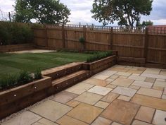 a backyard area with stone pavers, grass and wooden fenced in areas for seating