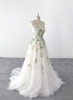 a white dress with flowers on it sitting on a mannequin