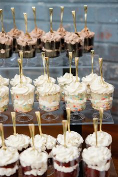 cupcakes and desserts are arranged on small clear trays with gold sticks sticking out of them