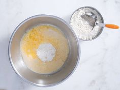 a metal bowl filled with flour next to a measuring cup on top of a white counter