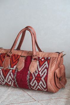 Handmade Moroccan Leather and Rug Duffel Bag/Weekender | Artisan Made Bag  Small/Medium Weekender / Travel bag / Duffel bag - this bag is made with dyed camel coloured leather and a gorgeous red kilim rug. It features a detachable long shoulder strap. Includes 2 inside pockets, and 2 small outside pockets.  Brought to you from the souks of Marrakech, we are a mixed Moroccan-British family run business who personally hand picked all of our artisan made products to bring them to London. We value q Bohemian Brown Weekender Bag For Everyday, Bohemian Leather Duffle Bag For Everyday Use, Brown Bohemian Weekender Bag For Everyday Use, Bohemian Satchel Bag For Trips, Bohemian Leather Bag For Trips, Bohemian Leather Bag For Travel, Bohemian Leather Tote Duffle Bag, Natural Color Travel Satchel Pouch, Bohemian Duffle Bag With Leather Handles For Daily Use