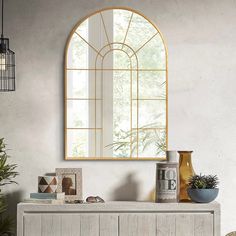 an arched mirror on the wall above a white dresser with plants and vases in front of it