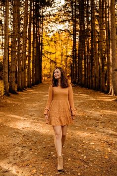 a woman in an orange dress walking down a dirt road surrounded by tall pine trees